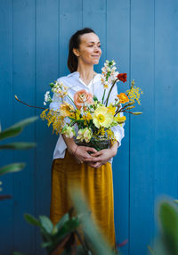 Woman in flowing yellow skirt and white shirt with bouquet in glass vase against the blue background