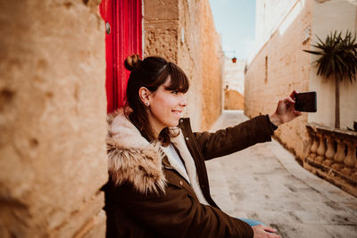 Close-up of woman using smart phone while sitting by door