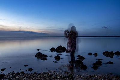 Rear view of woman standing in sea against sky during sunset