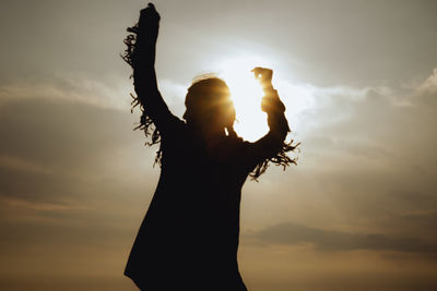 Silhouette woman with arms raised against sky during sunset