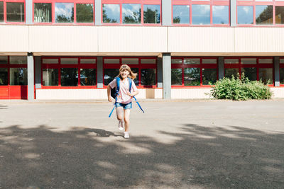 Contented schoolgirl with a backpack behind her back runs from school. the beginning of the holidays