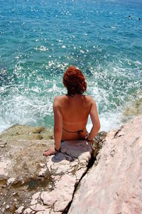 Rear view of woman sitting on rock by sea