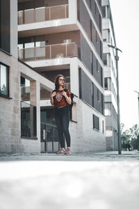 Portrait of smiling young woman standing against building in city