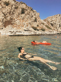 Young women swimming in sea against rock formation