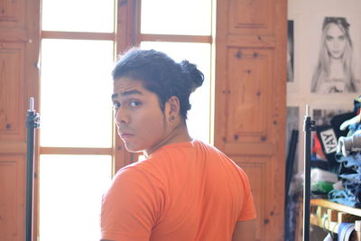 Portrait of young man looking away while standing against window