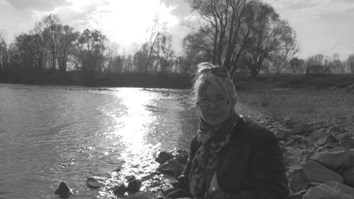 Woman sitting by lake against sky