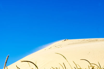 Low angle view of sand dunes against clear blue sky