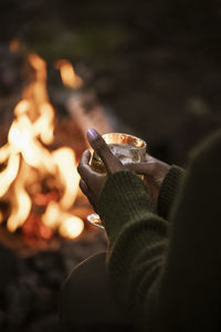 Woman holding glass of wine by campfire