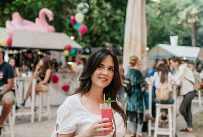 Beautiful young woman drinking strawberry mojito cocktail in park in city