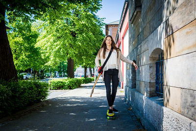 Full length of woman with guitar walking by building on sidewalk