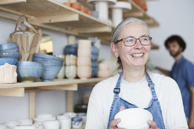 Smiling mature woman looking away while holding bowl in pottery class