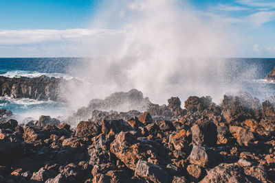 Waves splashing on rocks at shore against sky