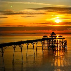 Silhouette built structure by sea against orange sky