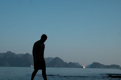 Silhouette man standing by lake against clear sky