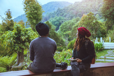 Man and woman sitting on retaining wall against trees