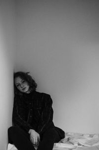 Woman sitting on bed against wall at home