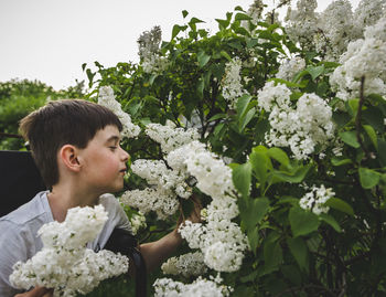 Boy with eyes closed smelling white flowers at park