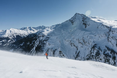 Man skiing on snowcapped mountains against clear sky