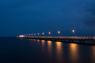 Illuminated bridge over sea against sky at night