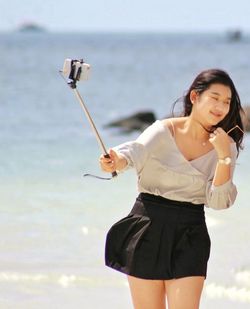 Woman taking selfie through smart phone while standing at beach