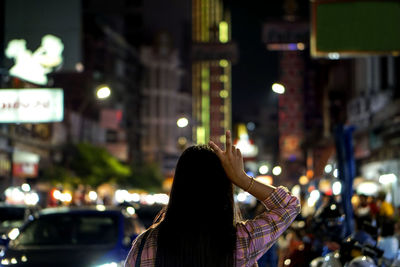 Rear view of woman walking on illuminated street at night