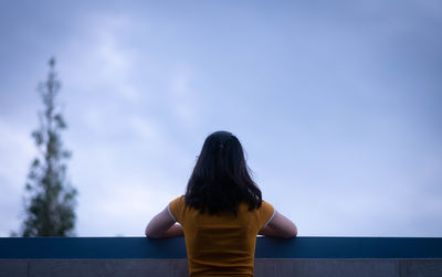 Rear view of woman standing by railing against sky