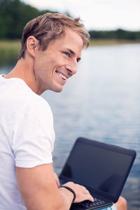 Smiling mature man using laptop while looking away at lake
