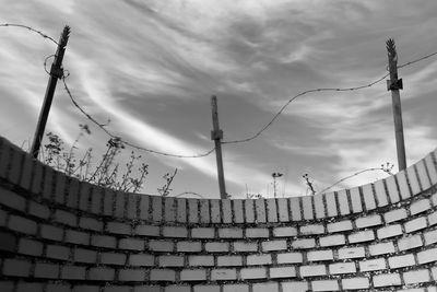 Low angle view of barbed wire on wooden post against cloudy sky