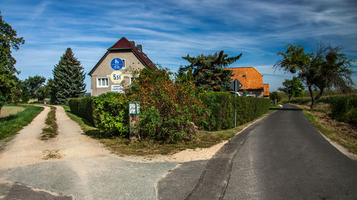 Road amidst trees and buildings against sky