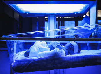 Baby suffering from jaundice lying under ultraviolet light in incubator