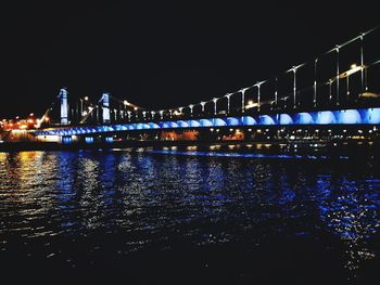 Illuminated bridge over river against sky at night