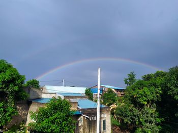 Rainbow over buildings and trees against sky