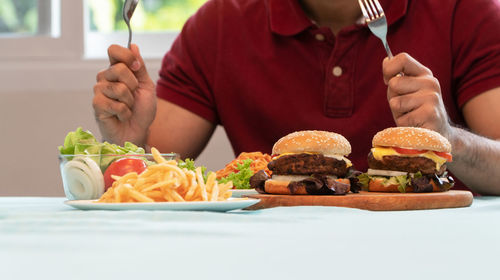 Young man holding knife and fork are ready to eating a hamburger, french fries, and spaghetti