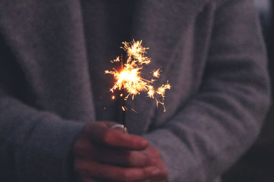 Midsection of person holding sparkler at night