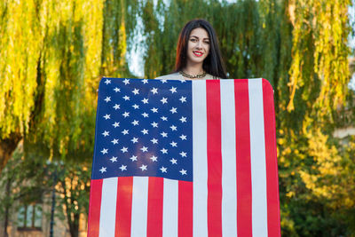 Portrait of smiling young woman standing against trees