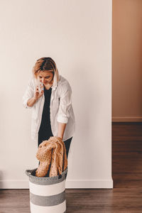 Young woman looking away while standing against wall at home