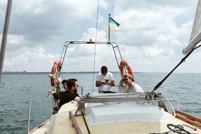 People sitting on sailboat in sea against sky