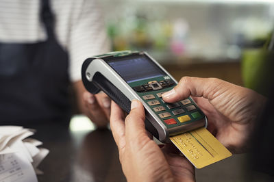 Midsection of female owner taking credit card payment from customer in cafeteria