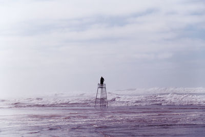 Man standing on lifeguard hut against sky at beach