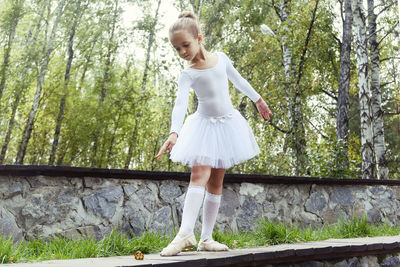 A little ballerina girl shows elements of choreography on a summer day on a path in the park