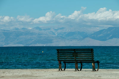 Empty bench by sea against sky