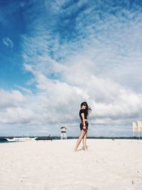 Side view of woman standing at sandy beach against cloudy sky