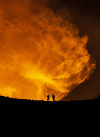 Silhouettes of anonymous travelers standing against orange fume of active volcano in iceland