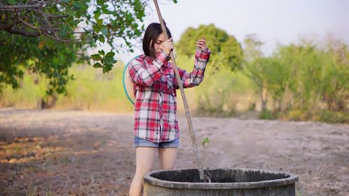 Young woman putting pole in well at farm