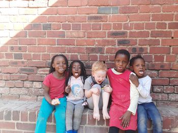 Portrait of smiling girl sitting against brick wall