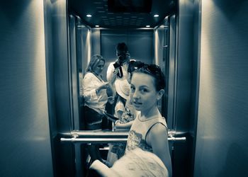 Portrait of girl against mirror with man and woman reflection while using camera in elevator