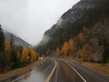 Road amidst trees and mountains against sky