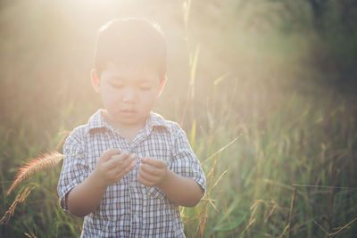 Portrait of happy boy standing on grassy field during sunny day