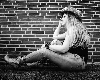 Young woman sitting against brick wall