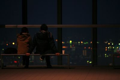 Rear view of couple sitting on bench at promenade during night